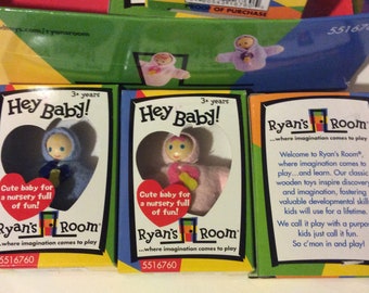 May include: Three boxes of Ryan's Room wooden toys. Each box features a different doll with a heart-shaped opening. The boxes are yellow, green, and blue with the text "Hey Baby!" and "Ryan's Room...where imagination comes to play".
