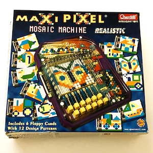 May include: A boxed Maxi Pixel Mosaic Machine toy. The box is dark blue with the words "Maxi Pixel" and "Mosaic Machine" in large letters. The toy itself is purple and clear, with colorful beads and yellow buttons. Includes 6 floppy cards with 12 design patterns.