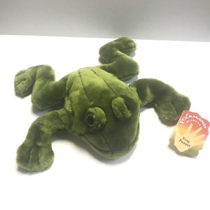 May include: Green plush frog hand puppet with black eyes. The puppet is lying on a white surface. The tag reads "Folkmanis Puppets Frog Puppet".