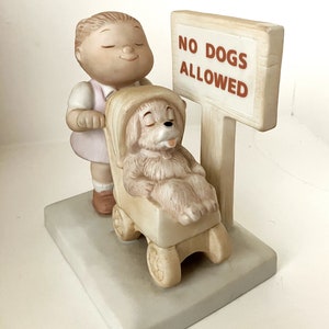 May include: A porcelain figurine of a child pushing a stroller with a dog inside. The sign reads "No Dogs Allowed".
