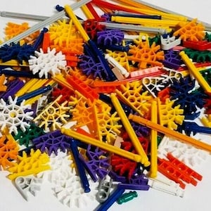 May include: A large pile of colorful plastic construction pieces, including rods, connectors, and gears. The pieces are in various shades of red, orange, yellow, green, blue, and purple.