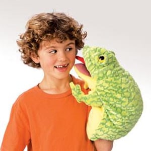 May include: A green and yellow plush frog hand puppet with a large, pink tongue sticking out. The puppet has a textured, bumpy surface and large, black eyes.