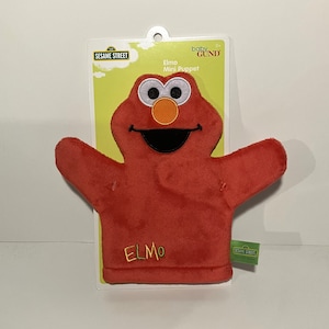 May include: Red Elmo hand puppet with a big smile and orange nose. The puppet is made of soft plush and has the words "Sesame Street" and "Elmo" embroidered on it.