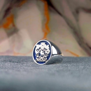 May include: A silver signet ring with a blue enamel crest featuring a lion and the text "Fidelidad y Honor".