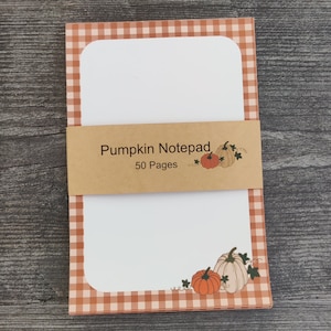 May include: A notepad with a gingham pattern in orange and white. The notepad has a brown label that says "Pumpkin Notepad 50 Pages". The notepad has a white interior with a pumpkin illustration.