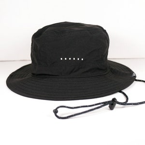 May include: A black bucket hat with a drawstring closure and a small white detail on the crown.