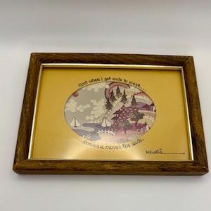 May include: A framed artwork with a brown wooden frame. The artwork features an oval-shaped image with a landscape scene, including sailboats, houses, and a rainbow. Text reads, "Just when I get ends to meet... Someone moves the ends."