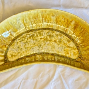 May include: A vintage, semi-circular serving dish with a unique glaze. The dish features a blend of yellow, gold, and brown hues, creating a marbled effect. The interior has a lighter, speckled pattern. This decorative piece is ideal for serving appetizers or displaying fruit.