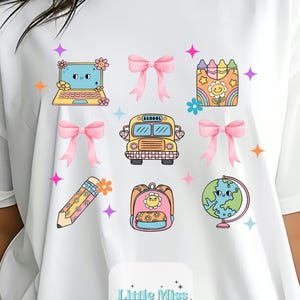 May include: White t-shirt featuring colorful school-themed graphics. Designs include a laptop, bows, a school bus, a pencil, a backpack, and a globe. The text "Little Miss Lovely Designs & Transfers" is at the bottom.