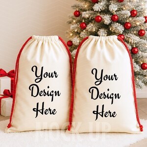 May include: Two off-white drawstring bags with red cords, each printed with "Your Design Here" in black script. The bags are set against a backdrop of a Christmas tree with red ornaments.