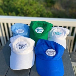 May include: Five baseball caps with the text "URANIUM $500" embroidered on the front. The caps are in different colors: blue, green, white, and two shades of blue.