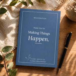 以下が含まれることがあります： 「Thank You for Making Things Happen」の文字と「Recognition」の文字が上部に書かれた、ネイビーブルーのノート。 金色のアクセントが付いた黒いペンが、木製の表面に置かれています。