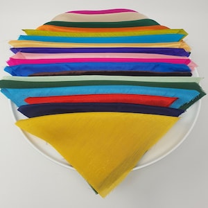 May include: A stack of fabric swatches in various colours, including yellow, red, blue, green, and pink. The swatches are arranged in a fan shape and are folded in half.