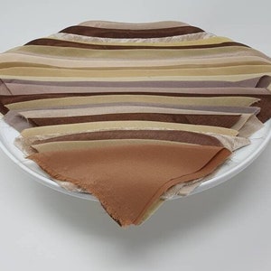 May include: A stack of fabric scraps in various shades of brown, beige, and cream. The fabric is arranged in a fan shape and is displayed on a white plate.