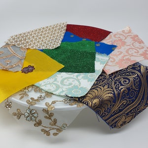 May include: Assortment of fabric swatches in various colours and patterns, including gold, blue, green, pink, and white. The swatches are arranged on a white plate.