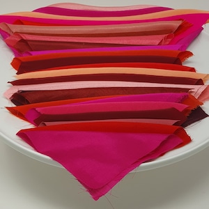 May include: A stack of fabric swatches in various shades of red, pink, and orange. The swatches are arranged in a fan shape on a white plate.