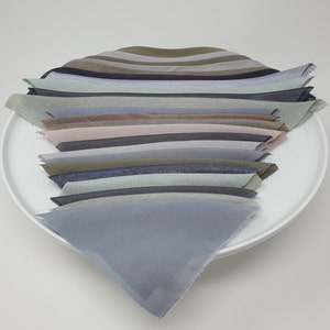 May include: A stack of 15 fabric swatches in various shades of blue, green, and brown. The swatches are arranged in a fan shape and are displayed on a white plate.