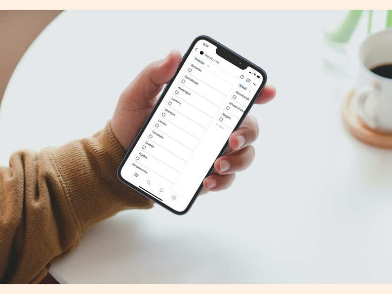 May include: A person's hand holding a smartphone displaying a grocery list app. The list includes items like bananas, asparagus, oranges, and bread.