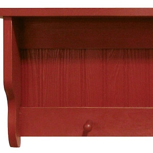 May include: A red wooden wall shelf with a top shelf, a lower shelf with two knobs, and a vertical paneled back. The shelf is painted a solid, deep red color. The design is simple and functional, suitable for storage or display.