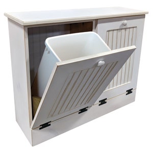 May include: White wooden trash can with a single door that opens to reveal a white plastic trash bin. The door has a white knob and black hinges. The trash can has a white top surface.