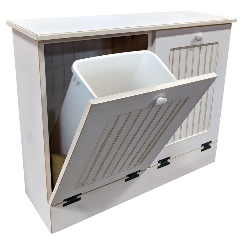 May include: White wooden trash can with a single door that opens to reveal a white plastic trash bin. The door has a white knob and black hinges. The trash can has a white top surface.