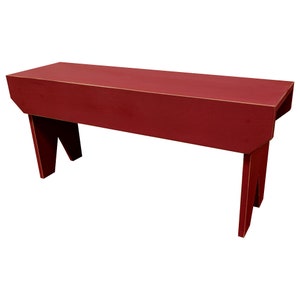 May include: A red wooden bench with a simple design and a distressed finish. The bench has a rectangular seat and two angled legs on each side.