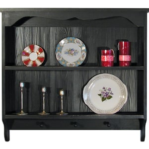 May include: Black wooden wall shelf with two shelves. The top shelf has three decorative plates and two candles. The bottom shelf has three candle holders and a decorative plate. The shelf has three hooks on the bottom.