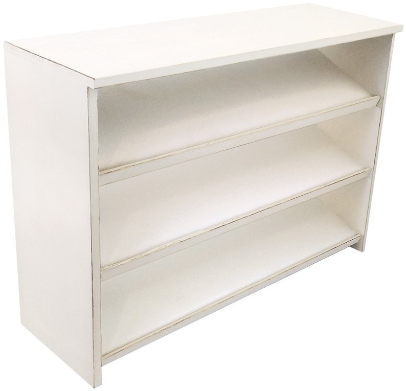 Op de afbeelding: Wit houten rek met drie planken. De planken zijn lichtjes naar voren gekanteld. Het rek heeft een verweerde witte afwerking.