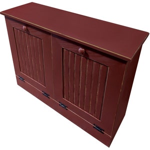 May include: A double-door red wooden trash can with a hinged lid and black metal hinges. The trash can has a distressed finish and is made of wood.
