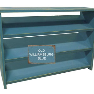 Op de afbeelding: Een blauwe houten plank met drie planken. De planken zijn schuin en hebben een gele rand. De plank is geverfd in een tint genaamd "Old Williamsburg Blue".