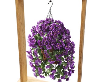 Puede incluir: Un soporte de madera marrón claro con una base rectangular y un letrero superior con la palabra Welcome en letra cursiva negra. Una cesta colgante llena de flores moradas vibrantes y hojas verdes cuelga del centro mediante un gancho de metal negro.