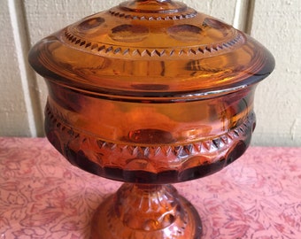May include: Amber glass candy dish with a pedestal base and a domed lid. The dish has a decorative pattern of small circles and a scalloped edge.