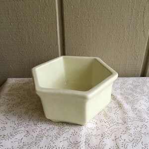 May include: A pale yellow hexagonal ceramic planter. The planter is empty and has a smooth, glossy finish.