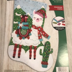 May include: A felt stocking kit featuring a Christmas llama with a red scarf and a cactus. The kit includes stamped felt, sequins, and beads. The stocking is 18 inches long.