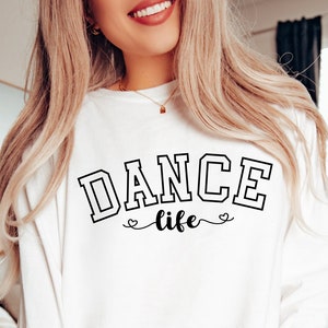 May include: White long-sleeve shirt with the text "DANCE life" in black lettering. The text is in a varsity style font with hearts on either side of the word "life".