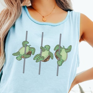 Op de afbeelding: Een lichtblauw tanktop zonder mouwen met een afbeelding van drie zeeschildpadden die aan een paal hangen. De tekst " Chambray" staat onderaan de afbeelding.