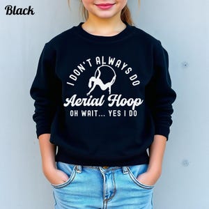 May include: Black sweatshirt with white text that reads "I DON'T ALWAYS DO Aerial Hoop OH WAIT... YES I DO". The sweatshirt is worn by a person wearing blue jeans. The word "Black" is in the top left corner.