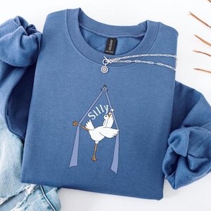 May include: A blue sweatshirt with a white goose graphic and the word "Silly" printed on it. The goose is holding onto a blue ribbon.