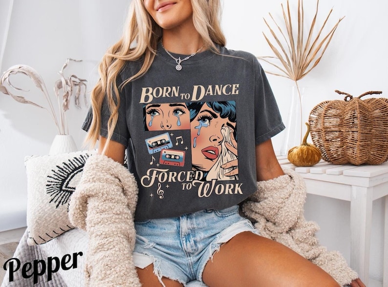 May include: A dark gray t-shirt with a vintage-style graphic of a woman crying with the text "Born to Dance Forced to Work" and cassette tape images.
