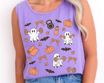 May include: A light purple sleeveless shirt featuring a repeating pattern of white ghosts lifting orange dumbbells, orange pumpkins, brown bats, orange bows, a yoga mat, a kettlebell, a water bottle, and small orange autumn leaves.
