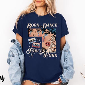 May include: A navy blue t-shirt with a graphic of a woman with tears in her eyes and the text "Born to Dance Forced to Work". The graphic also includes cassette tapes and musical notes.