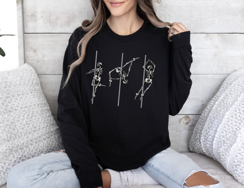 May include: Black sweatshirt featuring a graphic of three skeletons performing a pole dance. The skeletons are white and the poles are grey.