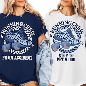 May include: Navy blue and white t-shirts with a graphic design. The design includes the text "RUNNING CREW MOST LIKELY TO PR ON ACCIDENT" and "RUNNING CREW MOST LIKELY TO STOP TO PET A DOG" with a running shoe and sunglasses.