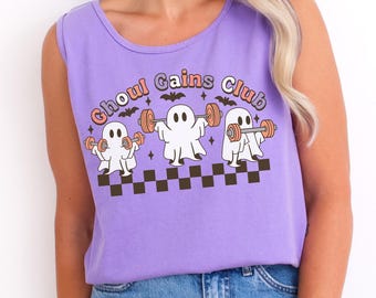 May include: A lavender tank top with the text "Ghoul Gains Club" and illustrations of weightlifting ghosts. The design includes bats, stars, and a checkered pattern at the bottom. The shirt is sleeveless and made of a soft material.
