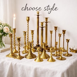 May include: A collection of brass candlesticks in various styles and heights, arranged on a white tablecloth. The phrase "choose style" is written in cursive script above the candlesticks. A lit candle and a vase of flowers are also present.