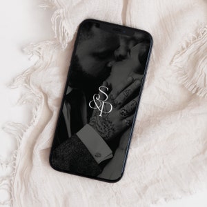 May include: A black and white photo of a couple kissing on a smartphone screen. The couple is wearing a suit and a dress. The screen also features a white monogram with the letters "S&P" intertwined.