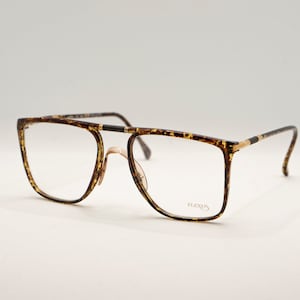 May include: Tortoise shell eyeglasses with gold accents and a square frame. The brand name "Flexon" is printed on the right lens.