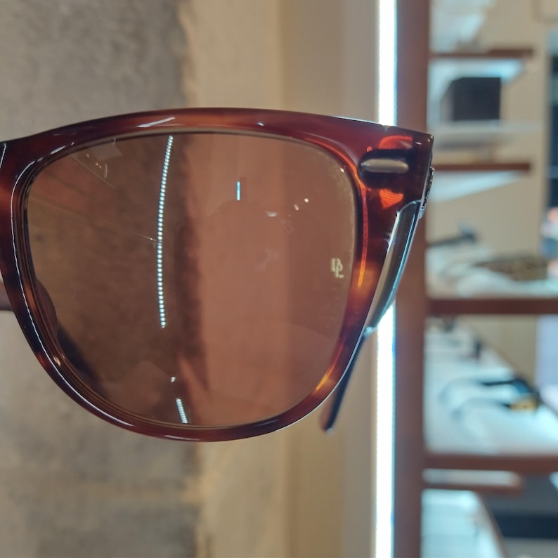 May include: Brown tortoise shell sunglasses with brown lenses. The sunglasses have a subtle sheen and a slight curve to the frame.