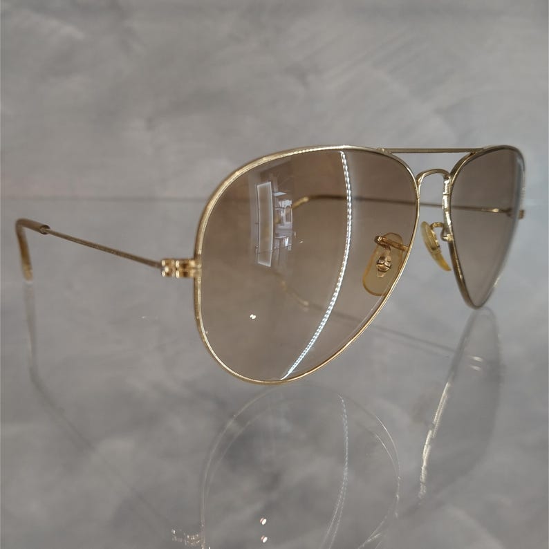 Puede incluir: Gafas de sol aviador doradas con lentes de degradado marr&oacute;n. Las gafas tienen un dise&ntilde;o cl&aacute;sico y est&aacute;n en buen estado.