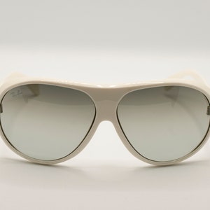 Puede incluir: Gafas de sol color crema con lentes degradadas. Las gafas tienen una montura gruesa y un dise&ntilde;o curvo. El logotipo de Ray-Ban es visible en la lente superior izquierda. Las lentes pasan de un tono m&aacute;s oscuro en la parte superior a uno m&aacute;s claro en la inferior.